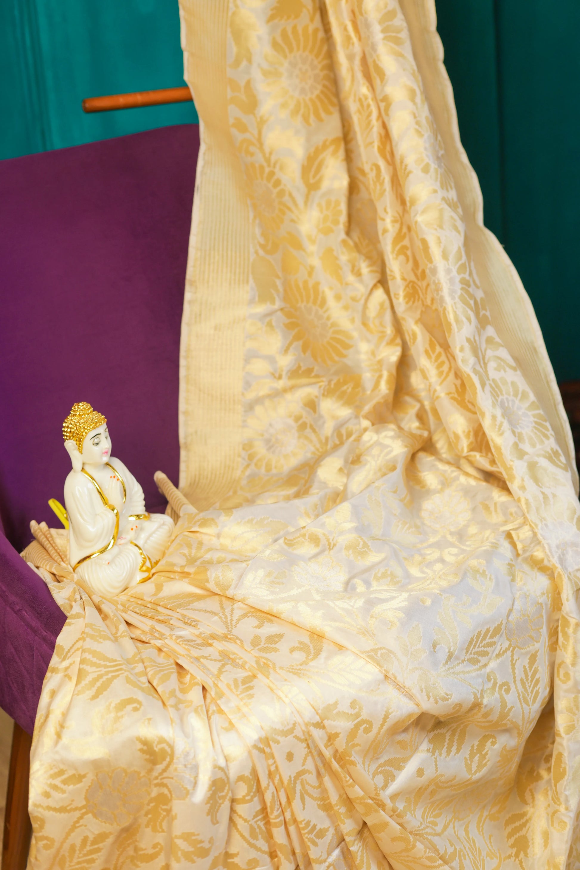 Gold and white embroidered fabric with a small statue on a purple surface
